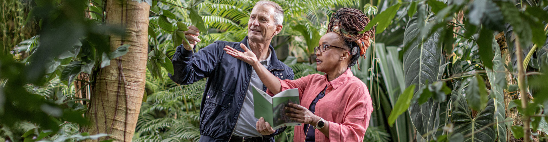 Two people walking through botanical gardens. The woman wears glasses and has a RONDO 3 audio processor behind her ear.