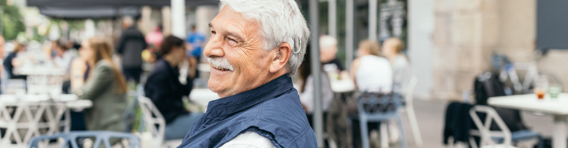 Ergonomic Design elderly man smiling while using SONNET 3 at a noisy café